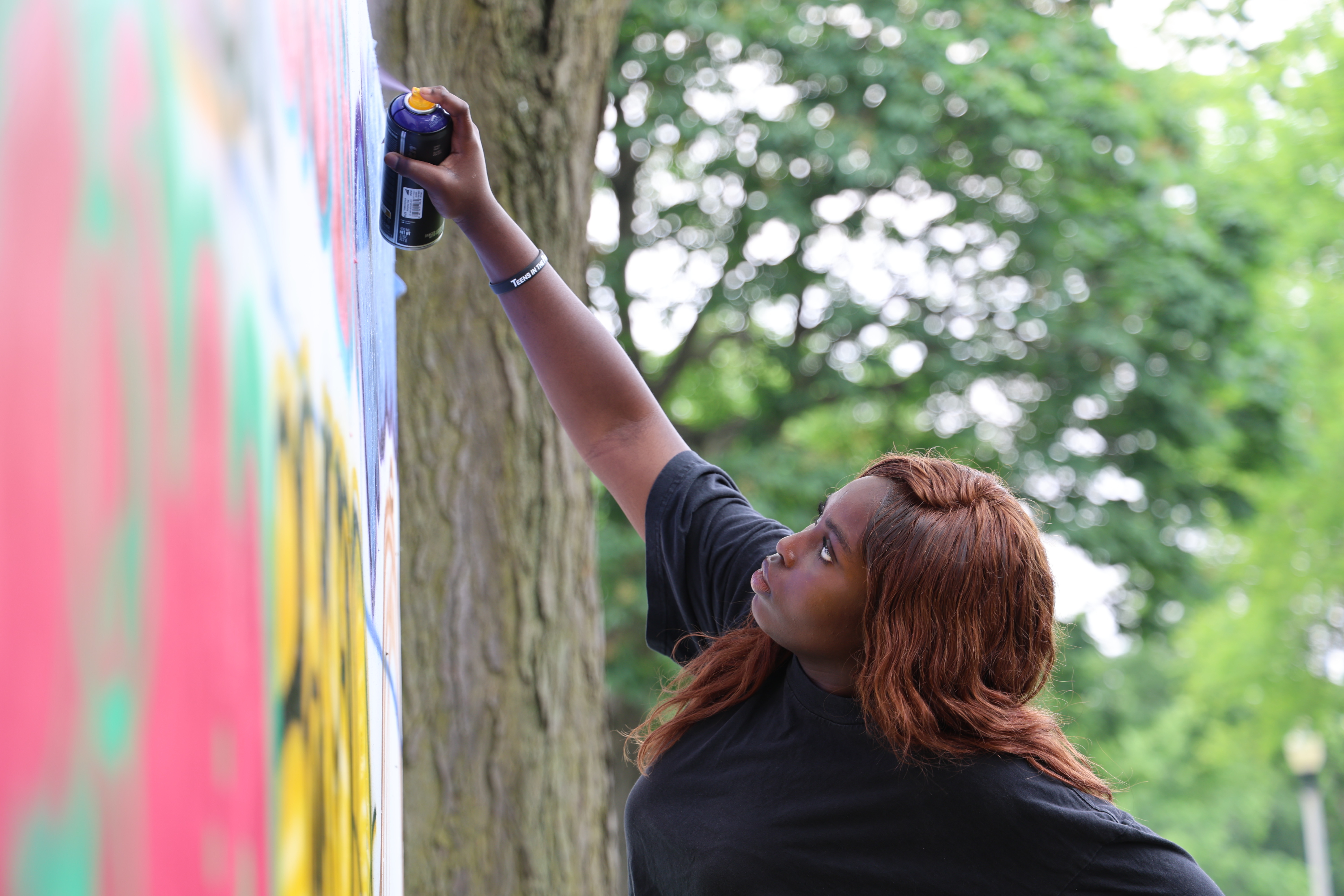 A young woman adds to a colorful mural with spray paint.
